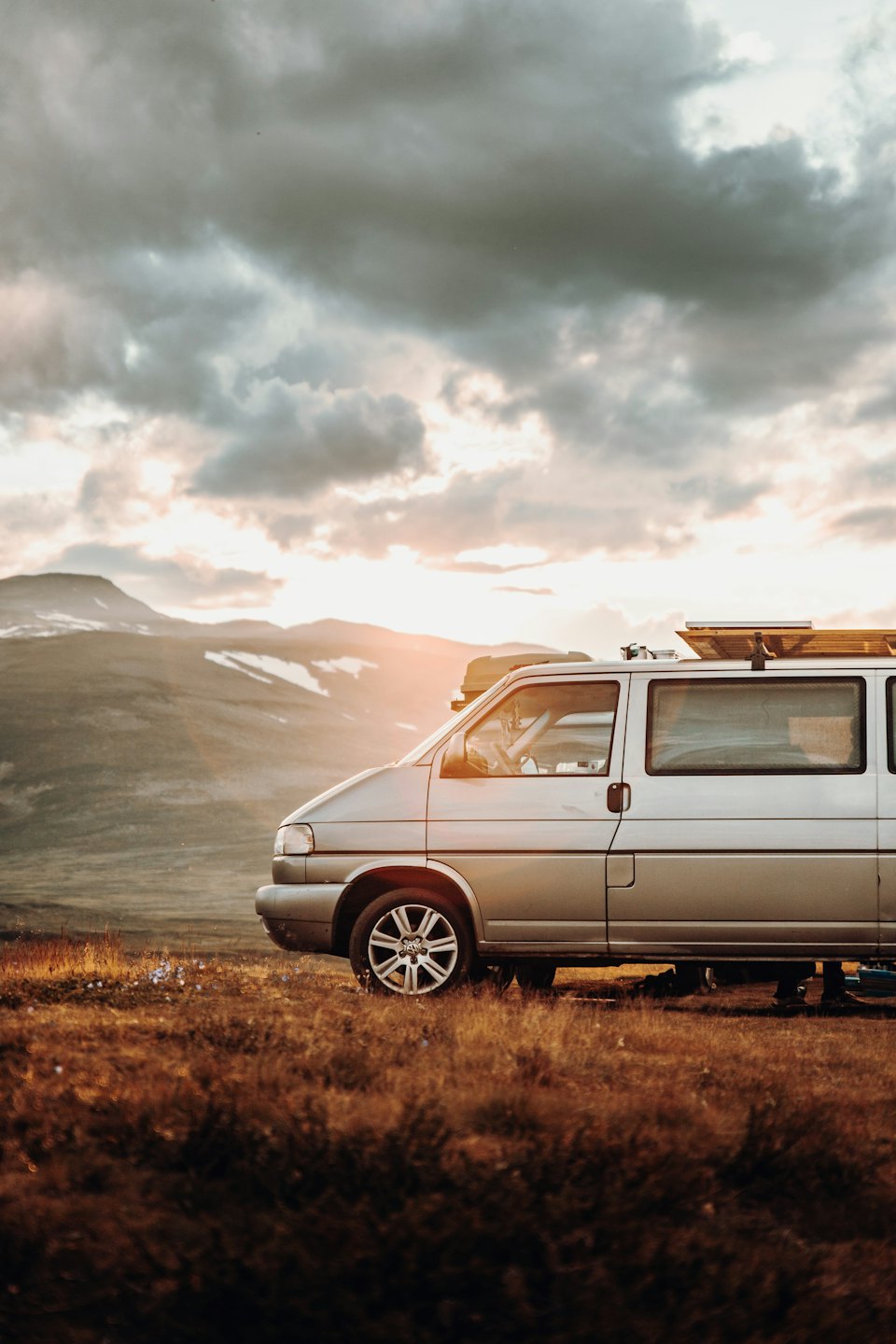 Un furgone camper argentato parcheggiato su un pendio erboso di montagna.