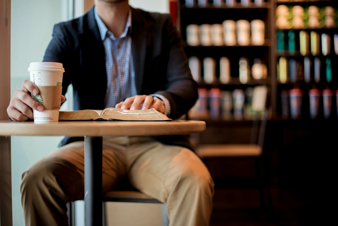 Un uomo legge un libro a un tavolino di un bar con un caffè.