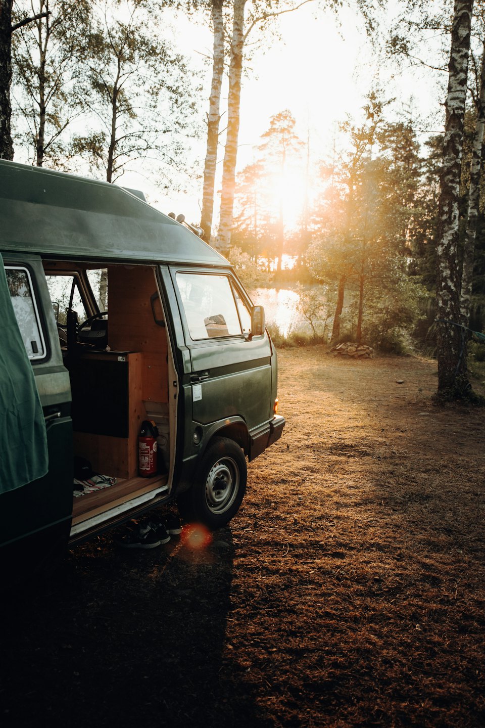 Furgone camper verde scuro parcheggiato con porta aperta al tramonto.
